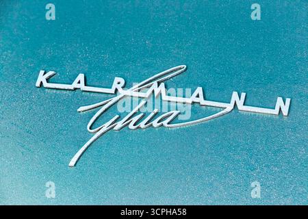 Nahaufnahme eines klassischen Karmann Ghia Chrom-Emblems auf einem blaublauen Metallic-Hintergrund, das das Oldtimer-Branding-Design zeigt Stockfoto