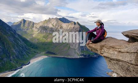 Ein einsamer Wanderer genießt atemberaubende Ausblicke vom Aussichtspunkt Ryten, mit Blick auf den atemberaubenden Strand Kvalvika und die dramatischen Berge in Lofoten, Norwegen an einem klaren Tag. Stockfoto