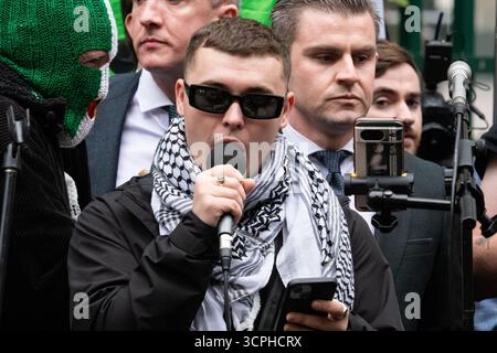 London, Großbritannien. 26. September 2025. Liam Óg Ó hAnnaidh, der unter dem Namen „Mo Chara“ mit irischem Hip Hop-Trio Kniescheibe auftritt, spricht bei einer Kundgebung vor dem Gericht an, nachdem der Sänger an einer Anhörung teilgenommen hatte, die feststellte, dass er nicht wegen des Terrorismusgesetzes angeklagt werden würde. Er wurde beschuldigt, eine Flagge zur Unterstützung der verbotenen Gruppe Hisbollah bei einem Konzert im Jahr 2024 angebracht zu haben. Er wies die Anschuldigungen ab und beschrieb sie als „politische Polizeiarbeit“ und als „Karneval der Ablenkung“ vom israelischen Krieg gegen Gaza, gegen den sich die Band wehrt. Quelle: Ron Fassbender/Alamy Live News Stockfoto