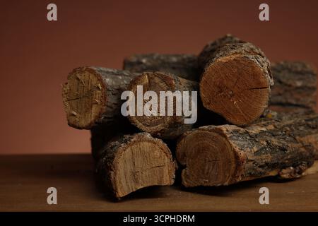 Haufen von geschnittenem Brennholz auf Holztisch vor braunem Hintergrund, Nahaufnahme Stockfoto