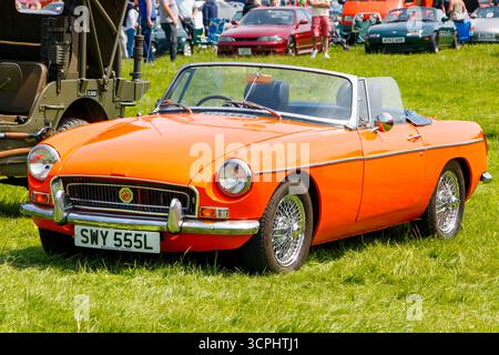 Leuchtend orange 1970er Jahre Vintage Cabrio MG Midget Sportwagen auf einer Oldtimer-Show mit Menschen und anderen Fahrzeugen im Hintergrund Stockfoto
