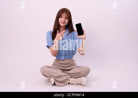 Junge Frau in lässigem Outfit zeigt Smartphone-Funktion mit freundlicher Präsentation für Social-Media-Inhalte und Marketing Stockfoto