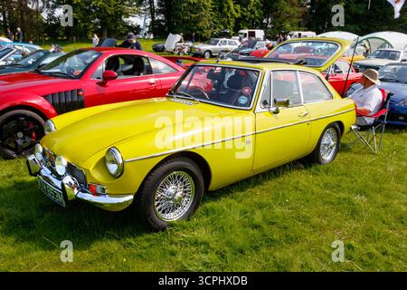 Ein gelber MGB-Sportwagen, der auf einer Oldtimer-Ausstellung auf einem grasbewachsenen Feld mit anderen Fahrzeugen im Hintergrund gezeigt wird Stockfoto