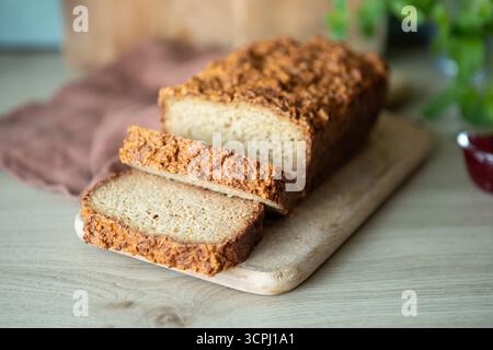 Frisch gebackenes Brot mit Vollkornbrot auf einem kleinen Holzschneidebrett. Der Brotlaib hat eine stark strukturierte, rustikale Kruste und eine weiche Innenseite Stockfoto