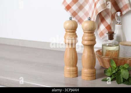 Salz, Pfeffermühlen, Flaschen mit Öl und Minze auf grauer Holztheke in der Nähe der weißen Wand, Nahaufnahme. Leerzeichen für Text Stockfoto