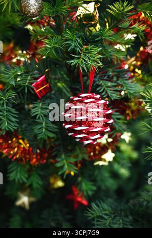Nahaufnahme eines verzierten Weihnachtsbaumzweigs mit glänzend roter Kugel, Lametta, goldenen und roten Verzierungen. Stockfoto