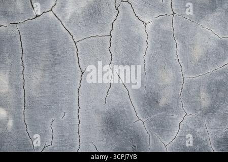 Grunge-Hintergrund mit Rissen an einer grauen Zementwand. Nahaufnahme einer alten Betonwand mit tiefen Rissen und verwitterter Oberfläche. Stockfoto