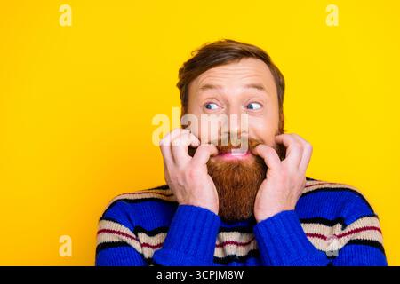 Amüsanter bärtiger Mann in einem gestreiften Pullover, der einen nachdenklichen Ausdruck vor einem hellgelben Hintergrund macht Stockfoto