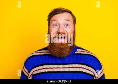 Fröhlicher bärtiger Mann mit einem hellen Lächeln in einem gestreiften Pullover vor einem auffälligen gelben Studio-Hintergrund, der sich fröhlich anfühlt Stockfoto