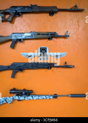 Eine moderne Aufklärungsdrohne, die Überwachung und Spionage repräsentiert, stand im Gegensatz zu einem Arsenal militärischer Angriffs- und Scharfschützengewehre an einer Mauer. Stockfoto