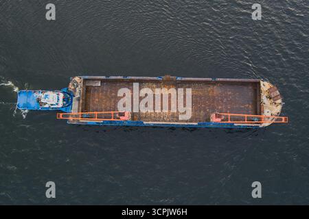 Draufsicht eines blauen Schleppers von oben nach unten, der einen großen, leeren Industriegutkahn über das Wasser schiebt. Stockfoto