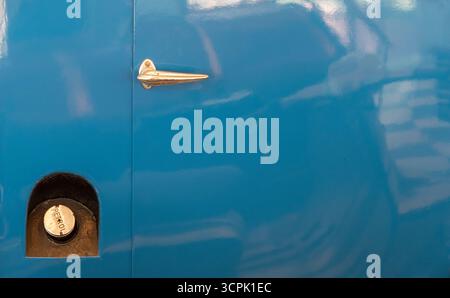 Ein leuchtend blauer Oldtimer verfügt über einen Tankdeckel aus glänzendem Metall und einen eleganten Türgriff. Das Ambiente hat ein nostalgisches Ambiente, das klassische Automobile betont Stockfoto