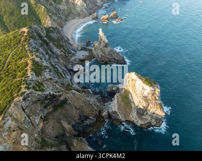 Aus der Vogelperspektive treffen Sie auf das türkisfarbene Meer in Praia da Ursa, wo goldener Sand die dramatischen Felsformationen küsst, Praia da Ursa, Lissabon, Stockfoto