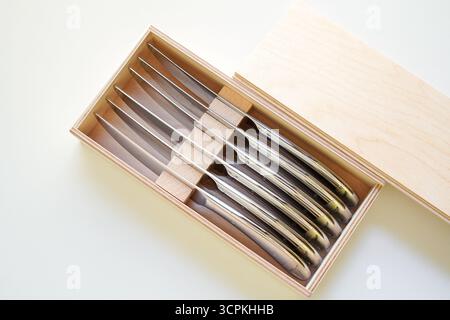 Steakmesser in einer Holzkiste auf weißem Hintergrund, direkt von oben gesehen Stockfoto
