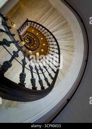 Wendeltreppe mit kunstvollem Eisengeländer und warmen Hängeleuchten von oben schaffen dramatische architektonische Perspektive und elegante historische Atmosphäre Stockfoto