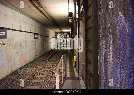 Bochum, Deutschland - 25. September 2025: Bahngleise, die tief in einen betonierten U-Bahn-Tunnel mit elektrischen Kabeln und Beleuchtung hineinreichen Stockfoto