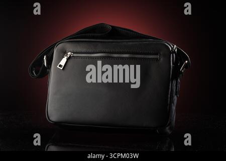 Dieses schwarze Modell der Tasche besticht durch ein schlankes Design mit einer auffälligen Reißverschlusstasche. Der dunkelrote Hintergrund sorgt für ein elegantes Erscheinungsbild, ideal für Werbe- oder Designpräsentationen. Stockfoto