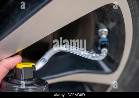 Selektiver Fokus auf chemisches Additiv, das aus einer Dose in einen Reifen gespritzt wird, um eine Panne zu reparieren Stockfoto