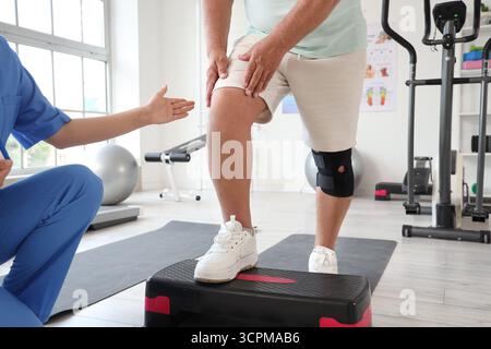 Seniorenübungen auf Stepper mit Therapeuten im Rehabilitationszentrum Stockfoto
