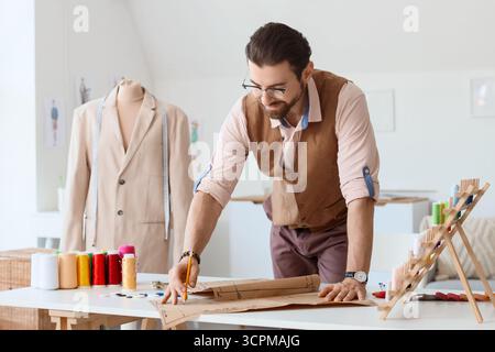 Männlicher Schneider, der mit Muster am Tisch im Atelier arbeitet Stockfoto