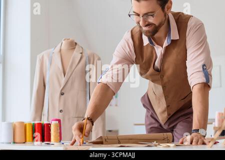 Männlicher Schneider, der mit Muster am Tisch im Atelier arbeitet Stockfoto