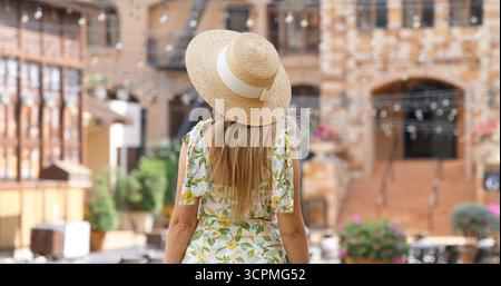 Frau in Sommerhut und Blumenkleid, die das mediterrane Dorf erforscht, Stockfoto