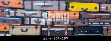 Eine Kollektion von Vintage-Koffern in verschiedenen Farben und Größen ist zusammengestapelt, um auf einem Markt im Freien auf einem hellen d ein Blickfang zu sein Stockfoto