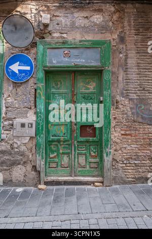 Verwitterte grüne Tür mit Graffiti an der alten Ziegelmauer. Urbaner Verfall, Vintage-Eingang, verstörte Farbe, traditionelle Architektur, historisches Viertel Stockfoto