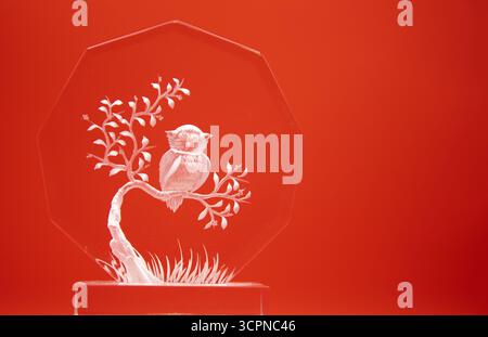 Dekoratives Glasschmuck mit einer auf einem Ast sitzenden Äuleneule auf rotem Hintergrund. Stockfoto