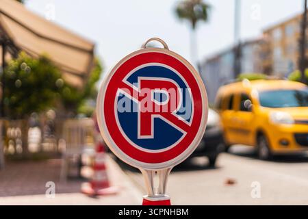 Ein rot-blaues Schild ohne Parken ist gut sichtbar auf einer sonnigen Stadtstraße. Im Hintergrund sind ein gelbes Taxi und geparkte Fahrzeuge zu sehen Stockfoto
