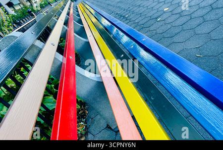 Farbenfrohe Holzbänke in Gradient Row entlang des gepflasterten Weges Stockfoto
