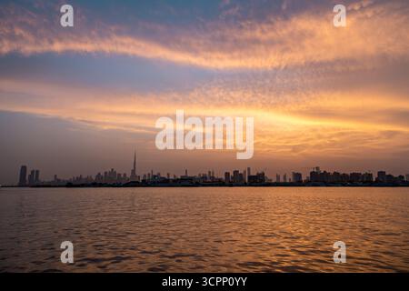 Blick auf die Skyline bei Sonnenuntergang auf Dubai und den berühmten Burj Khalifa vor einem orangefarbenen Himmel, der sich im Flusswasser spiegelt Stockfoto
