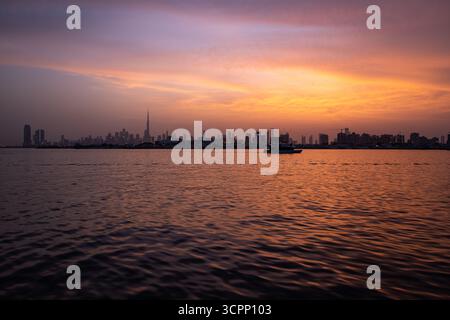 Goldener Sonnenuntergang in Dubai mit Skyline-Hintergrund von Dubai, Wellen im Wasser - Blick vom Bach Hafen dubai Stockfoto