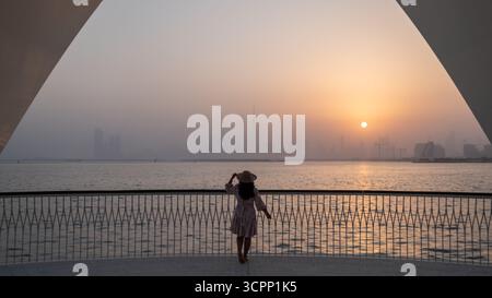 Silhouette eines Mädchens, das die Skyline von Dubai zur goldenen Stunde bewundert, malerischer Blick vom Hafen von Dubai Creek im Winter - horizontales Stockfoto Stockfoto