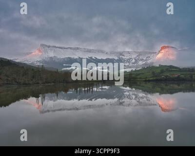 Snowy Mountain Reflection at Twilight – dramatische Winterlandschaft mit einem schneebedeckten Berg, der sich perfekt auf einem ruhigen See mit zwei Gipfeln spiegelt Stockfoto