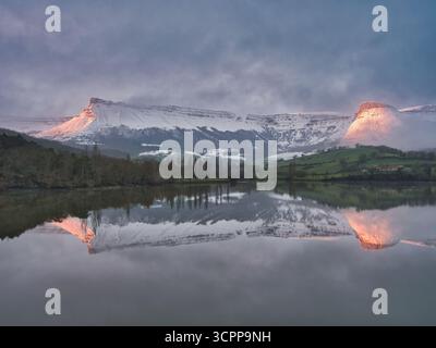 Snowy Mountain Reflection at Twilight – dramatische Winterlandschaft mit einem schneebedeckten Berg, der sich perfekt auf einem ruhigen See mit zwei Gipfeln spiegelt Stockfoto