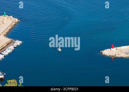 Kleine Boote, die auf einem ruhigen blauen See in den Hafen einfahren, führen die grünen und roten Boje Schiffe in den Hafen. S-förmige Welle, die vom Boot auf dem Wasser gebildet wird Stockfoto