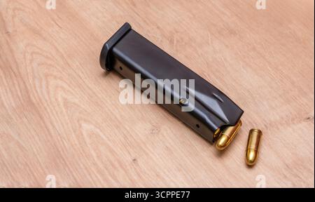 Eine Nahaufnahme eines geladenen Gewehrmagazins mit mehreren Kugeln, die auf eine Holzoberfläche auslaufen. Ein Stillleben von Pistolenklemme mit Munition. Stockfoto