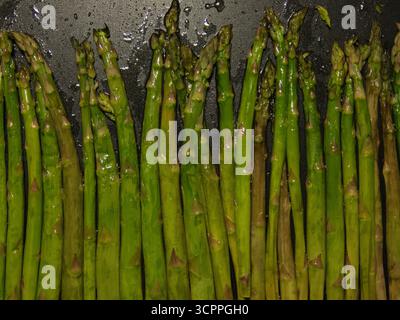 Gegrillter grüner Spargel-Gemüsedetail – Vollformatansicht von glänzenden, gegrillten grünen Spargelstangen auf einer dunklen Kochfläche. Konzept für h Stockfoto