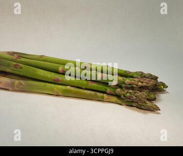 Fresh Green Spargelspitzen Nahaufnahme – Makroaufnahme von rohen grünen Spargelspitzen vor einem leuchtend kalkgrünen Hintergrund und weißer Oberfläche. Konzept für Stockfoto