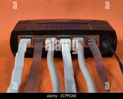 Router mit Ethernet-Kabeln orangefarbener Hintergrund – Nahaufnahme der Rückseite eines schwarzen Netzwerk-Routers mit mehreren weißen RJ45-Ethernet-Kabeln. Co Stockfoto