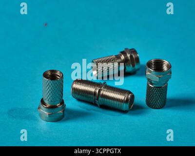 F-Typ Koaxialsteckverbinder Blauer Hintergrund – drei glänzende F-Typ Koaxialkabelsteckverbinder aus Metall, verstreut auf einem hellen türkisblauen Hintergrund. Konzentrieren Sie sich auf Stockfoto