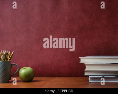 Vintage-Schreibtisch mit Kopierraum - Gläser, Apfel und Bleistifte in einem strukturierten Becher auf einem Bücherstapel und Holztisch. Bildungskonzept mit Rot Stockfoto