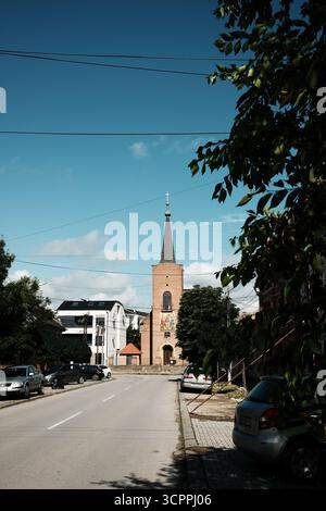 Blick auf die Straße, die zu einem hohen orthodoxen Kirchturm führt. Serbien, Vrsac - 22. Mai 2025. Stockfoto