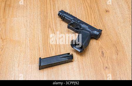 Pistole mit entferntem Choke vor dem Holz. Moderne Pistole auf strukturierter Holzoberfläche, begleitet von einem abnehmbaren Magazin. Stockfoto