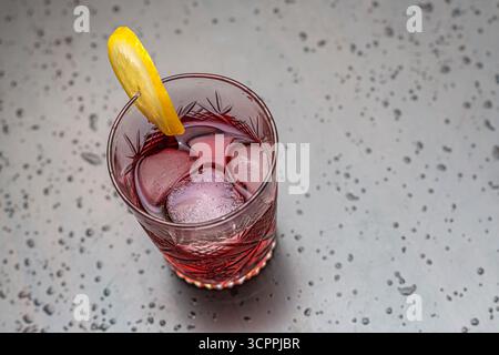 Erfrischender roter Cocktail mit Eis- und Zitronengarnitur. Eine Nahaufnahme eines erfrischenden roten Cocktails, serviert in einem alten Kristallglas. Selektiver Fokus. Stockfoto