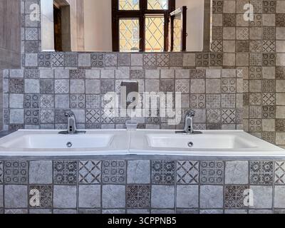 Modernes Badezimmer mit zwei Waschbecken, Spiegeln und dekorativen geometrischen Fliesen, die zeitgenössisches Design und klare Linien bieten Stockfoto