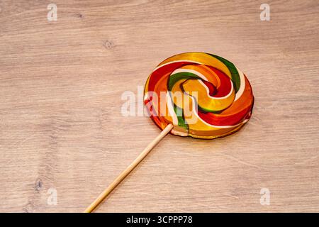 Bunte Süßigkeiten. Farbenfroher Lutscher mit roten, orangen, grünen, gelben und weißen Tönen auf einer warmen Holzoberfläche. Im Zusammenhang mit der Kindheit. Stockfoto