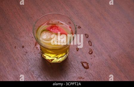 Dieses verführerische Bild zeigt ein Glas, das mit einem gelben Getränk gefüllt ist und mit frischen Erdbeerscheiben und Eiswürfeln geschmückt ist. Perfekt für Menüs. Stockfoto