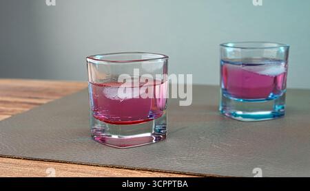 Zwei quadratische Gläser gefüllt mit rosafarbener Flüssigkeit und Eiswürfeln auf Lederoberfläche. Eine minimalistische und elegante Komposition. Selektiver Fokus. Stockfoto